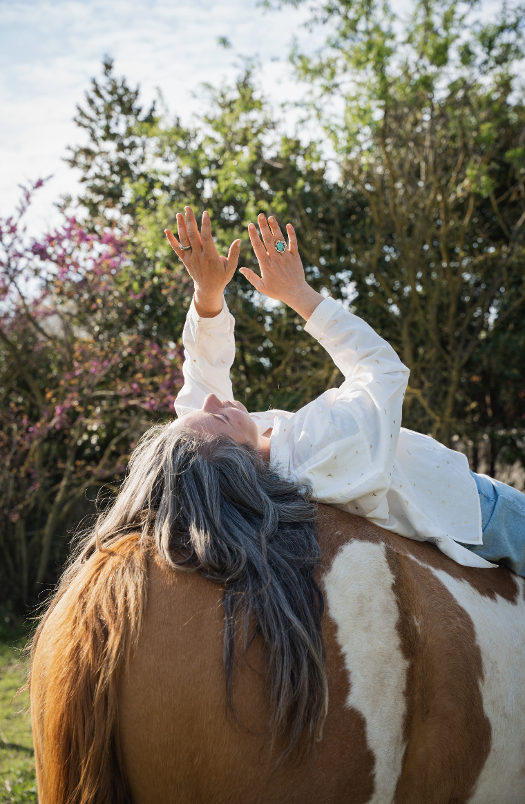 Femme allongée sur un cheval, bras tendus vers le ciel